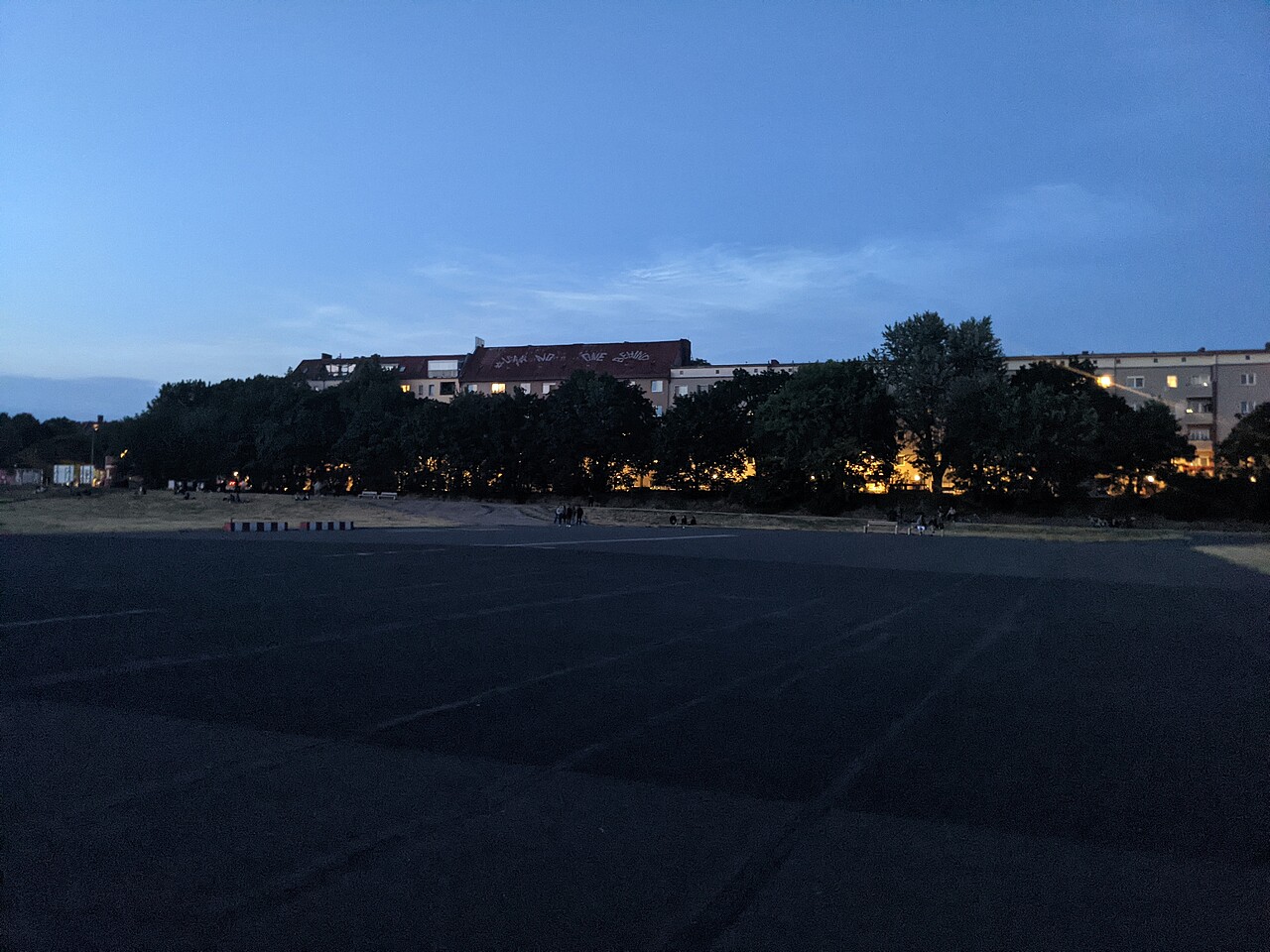The end of the Tempelhofer Feld runway in the evening. Lanterns shine through the trees on Okerstraße.