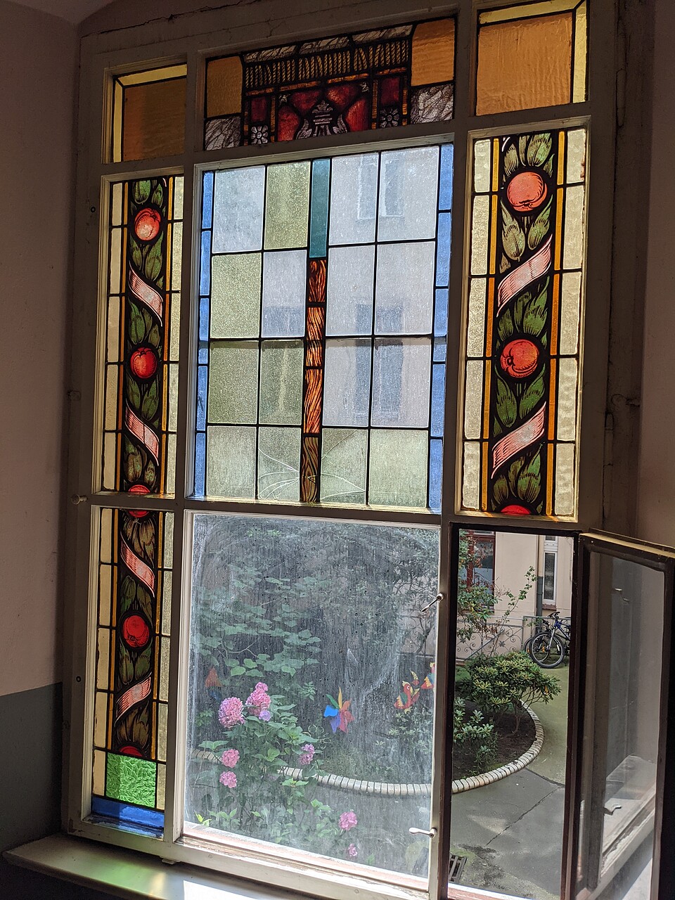 Colorful stained glass in the staircase of a Berlin apartment building. The view goes into the courtyard, a small part of the window is open.
